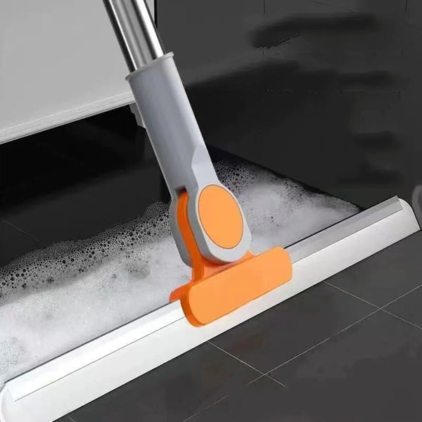 An orange silicone squeegee broom with an aluminum handle is shown cleaning a floor.