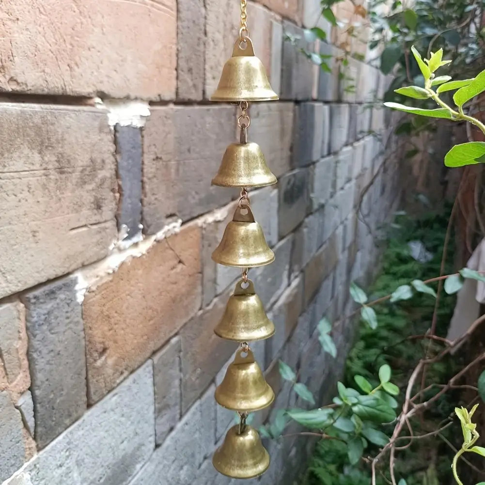 A vertical arrangement of brass metal wind chimes hanging against a textured brick wall.