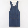 A dark blue denim apron with chest pockets hanging on a white hanger.
