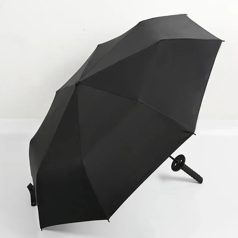 A black folding katana sword umbrella is shown angled on a white surface.