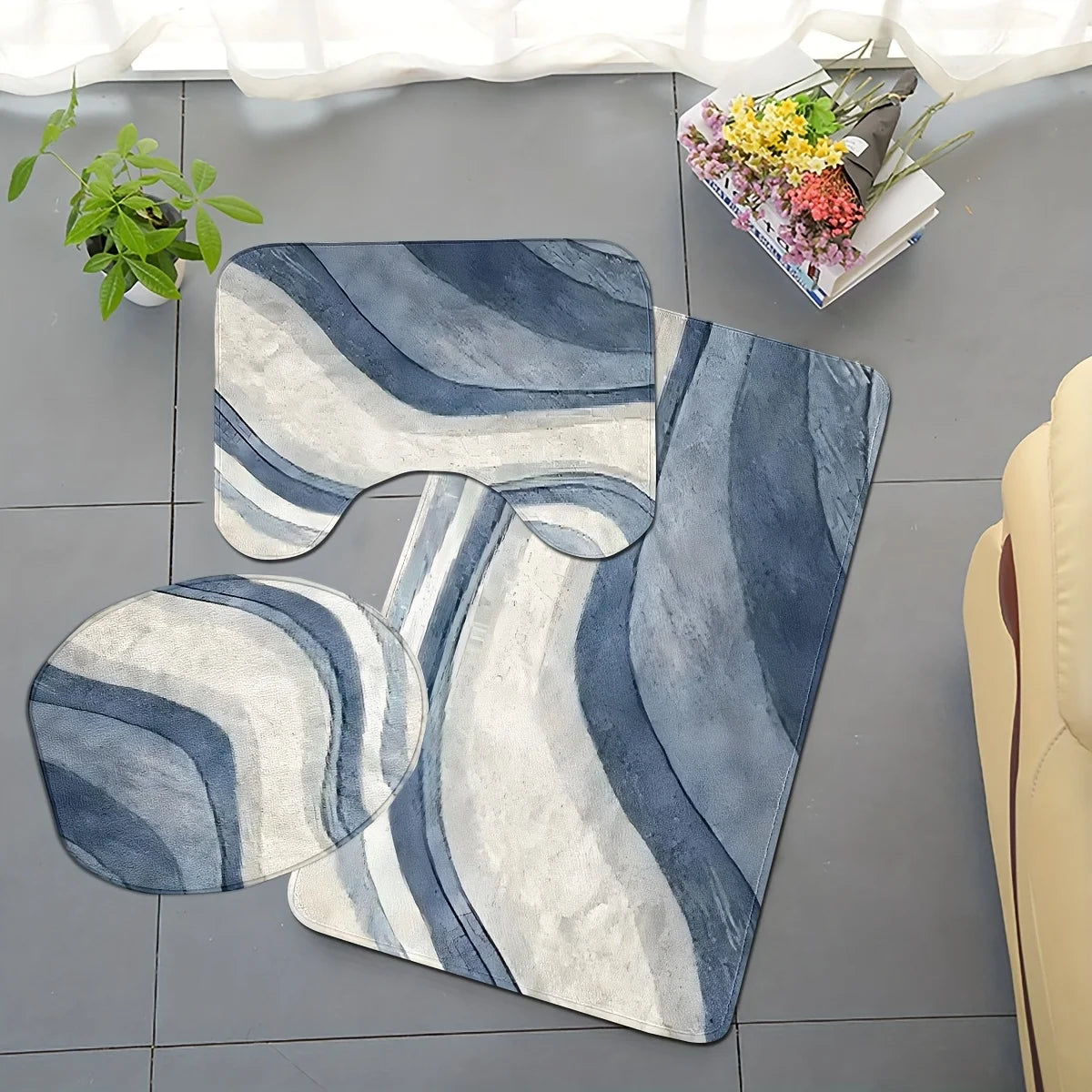 A set of three soft non-slip bathroom rugs featuring blue and white wavy stripes on a gray floor.