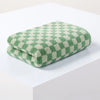 A stack of green and cream plaid cotton bath towels resting on a white surface.