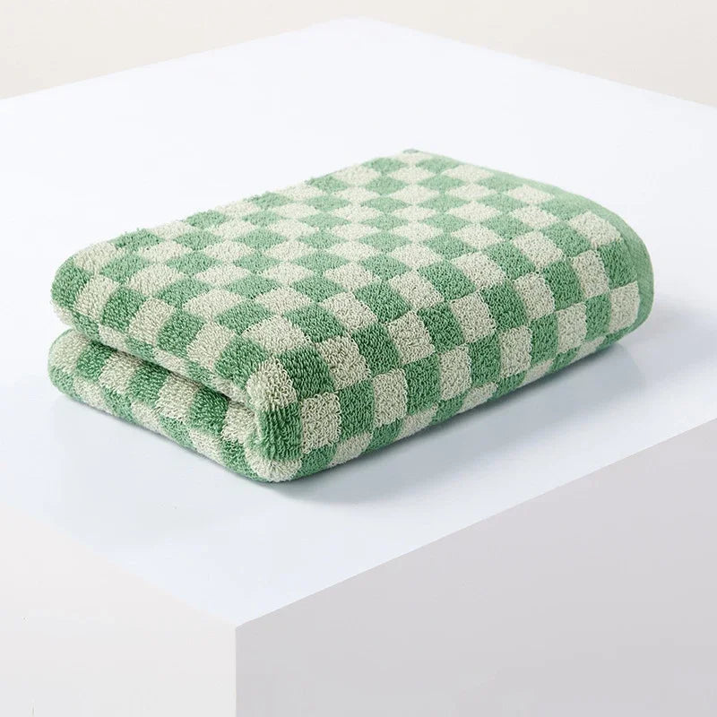 A stack of green and cream plaid cotton bath towels resting on a white surface.