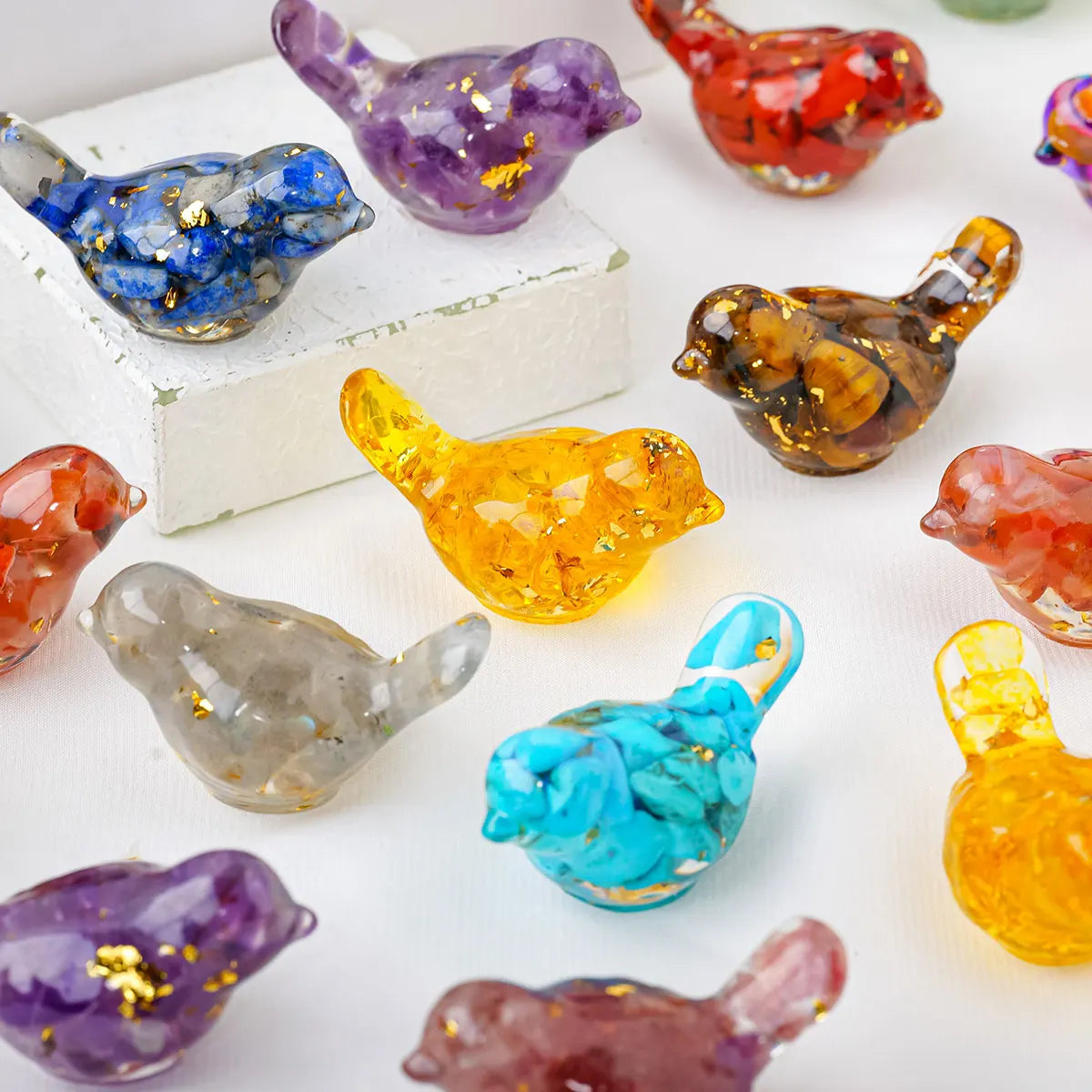 A collection of colorful natural crystal bird statues in various shades including purple, blue, orange, and yellow.