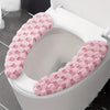 A white toilet seat with a pink, fluffy washable cushion cover installed.