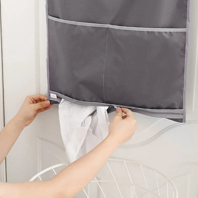 A person is hanging a gray foldable laundry basket organizer on a white door, demonstrating its use.