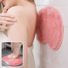 A pink reusable silicone foot scrub brush is shown hanging on a white tile wall next to a person's arm.