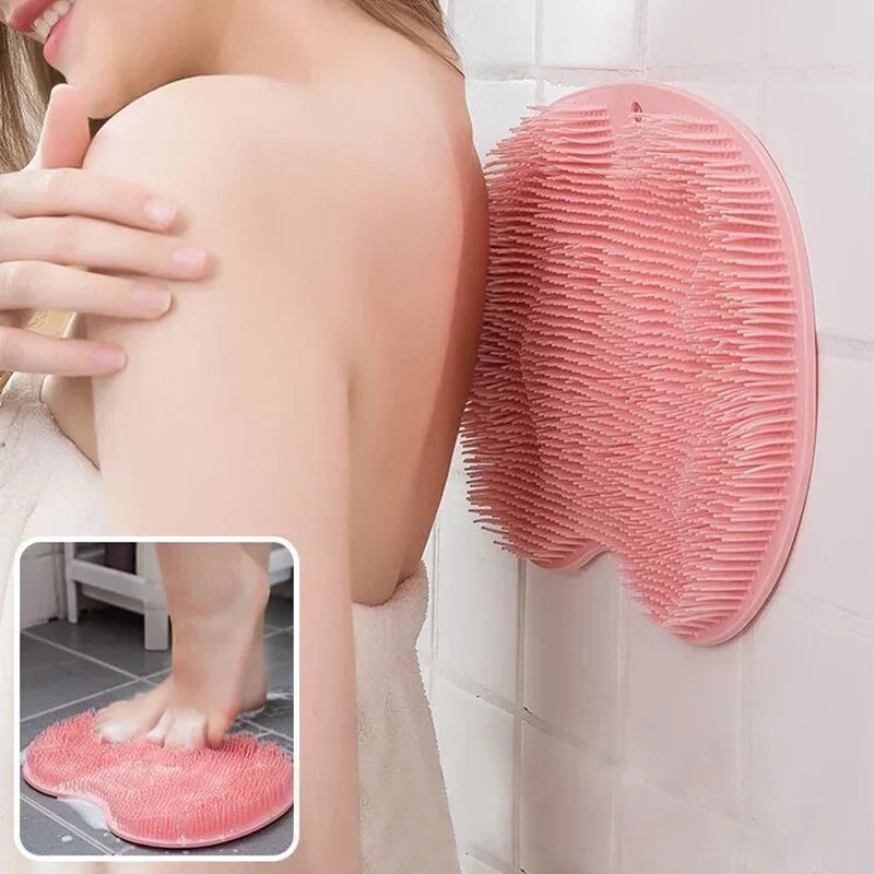 A pink reusable silicone foot scrub brush is shown hanging on a white tile wall next to a person's arm.
