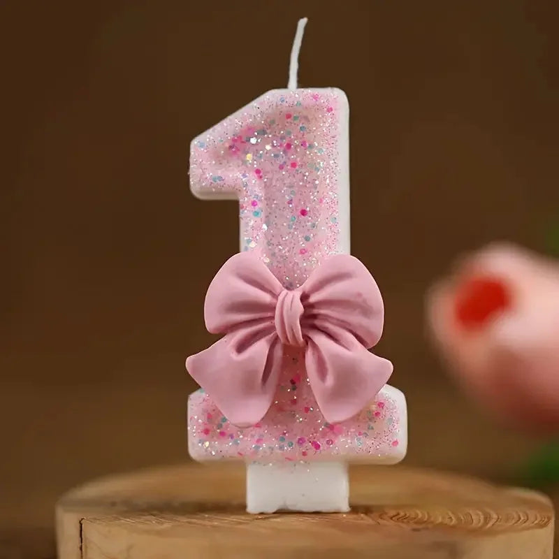 A glitter number one candle decorated with pink glitter and a pink bow on a wooden surface.