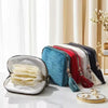 A collection of elegant velvet jewelry storage bags in various colors and styles with tassels displayed on a white marble sur