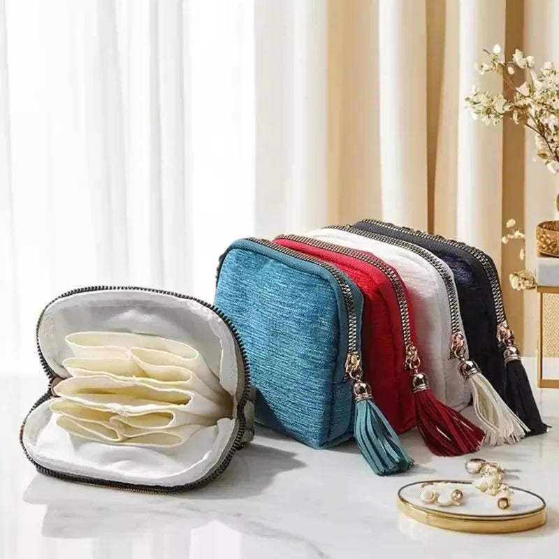 A collection of elegant velvet jewelry storage bags in various colors and styles with tassels displayed on a white marble sur