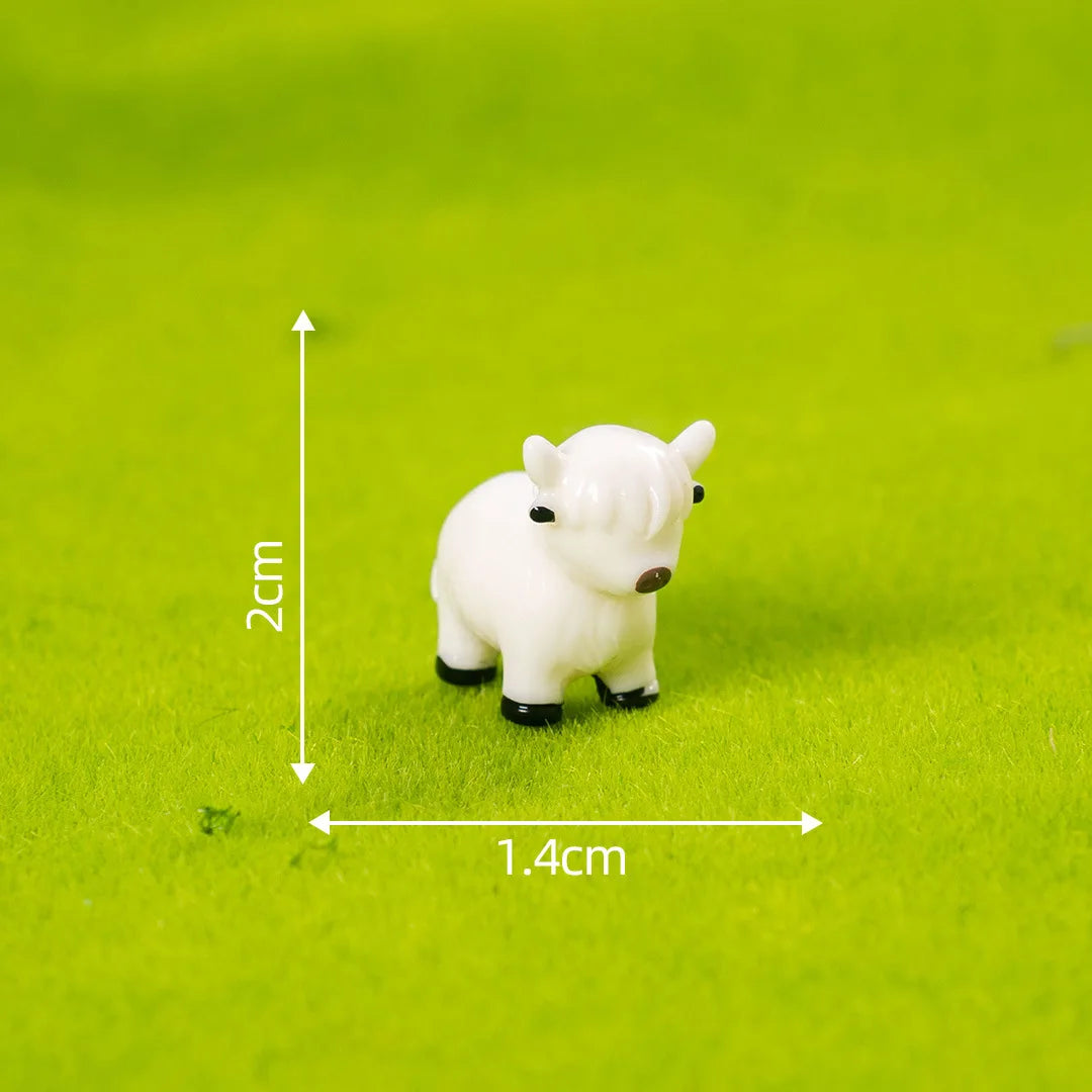 A white resin figurine of a Highland cow standing on green grass, shown with a scale marker.