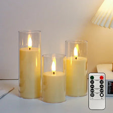 Tres velas de tres pilares en portavelas de vidrio exhibidas sobre una superficie blanca junto a un temporizador remoto para 