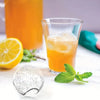 A glass of orange juice with ice and a silicone mold for making ice cubes is displayed on a white surface.