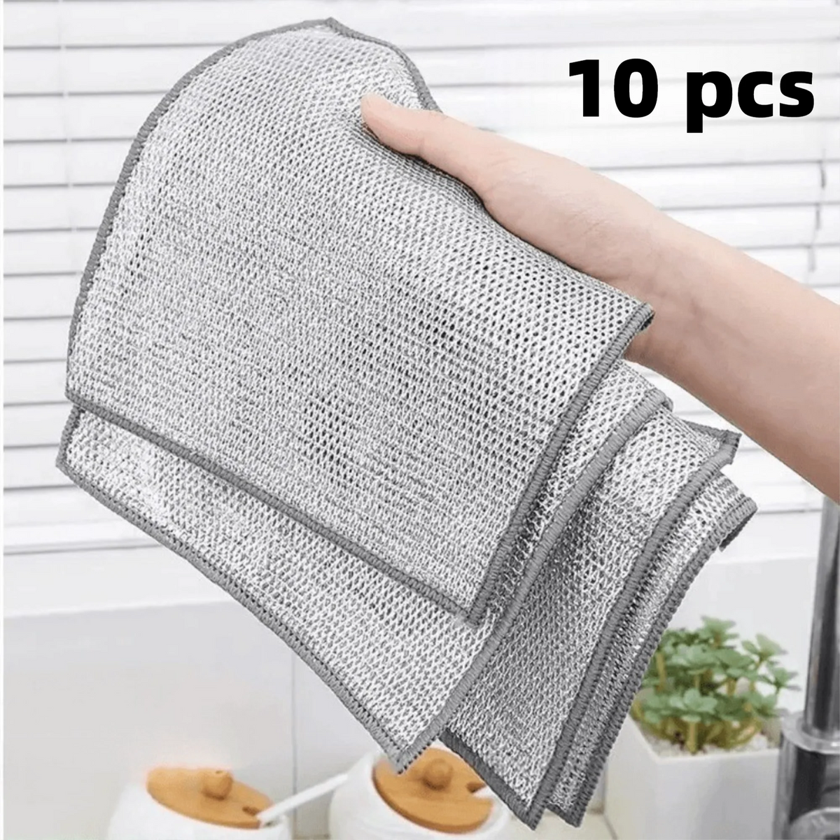 A hand is holding a stack of ten gray non-stick wire cleaning dish rags.