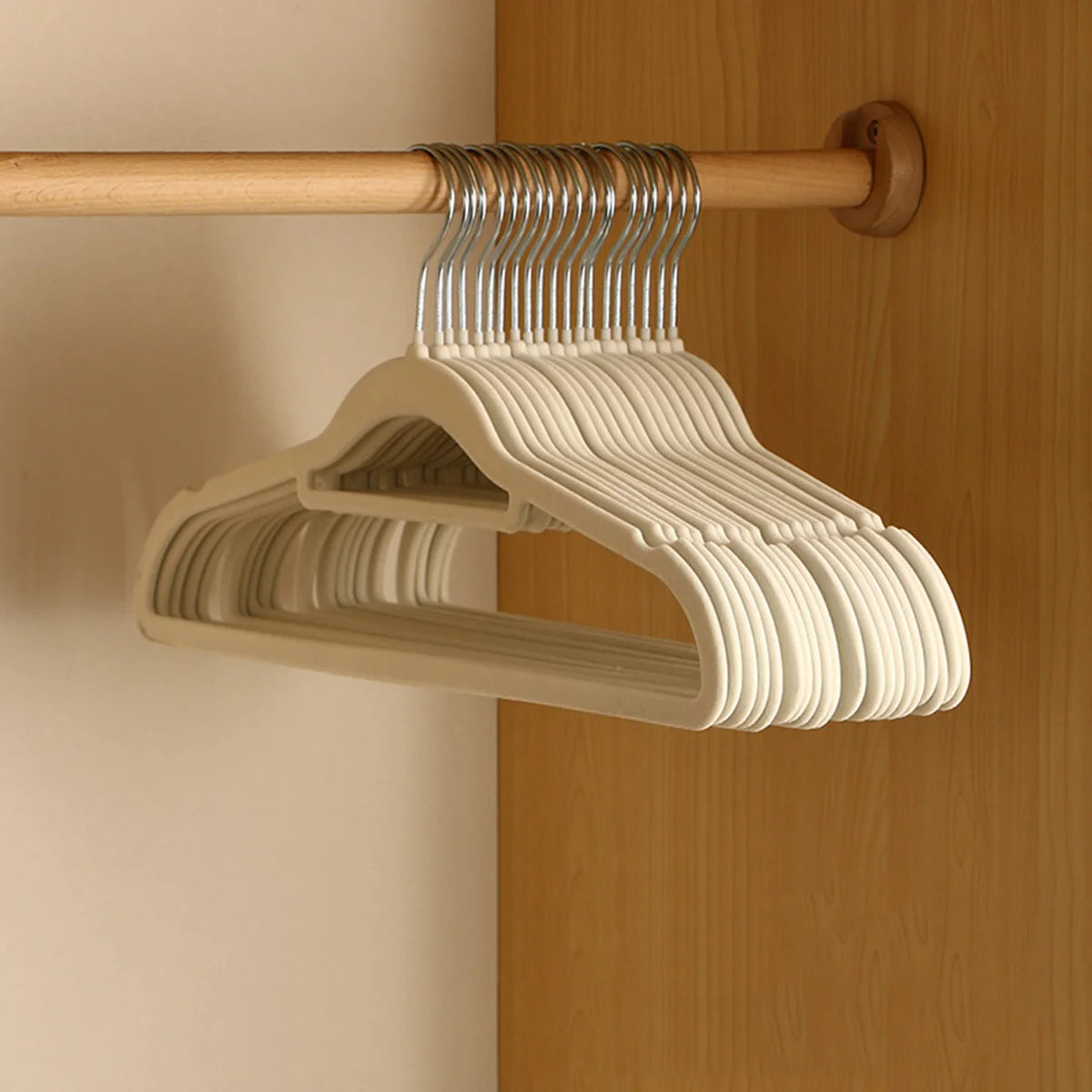 A set of white velvet slim hangers hanging from a wooden rod on a light wood cabinet door.
