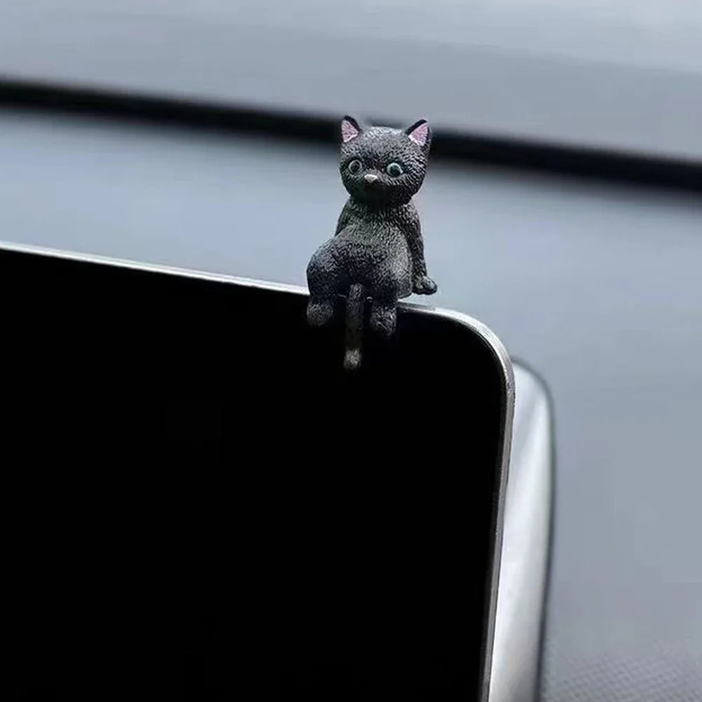 A small, dark gray cat figurine is perched on the edge of a black device.