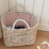 A vintage floral storage basket with a woven handle sits on a wooden surface.