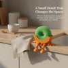 A cute, green sponge holder with wooden legs sits on a kitchen counter next to a white cutting board.