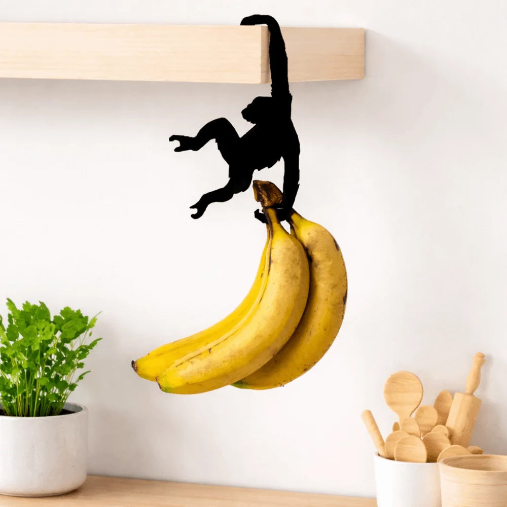 A black monkey silhouette hangs from a wooden shelf, next to a bunch of yellow bananas.