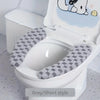 A white toilet features a grey short style seat cushion cover with a cute bear design.
