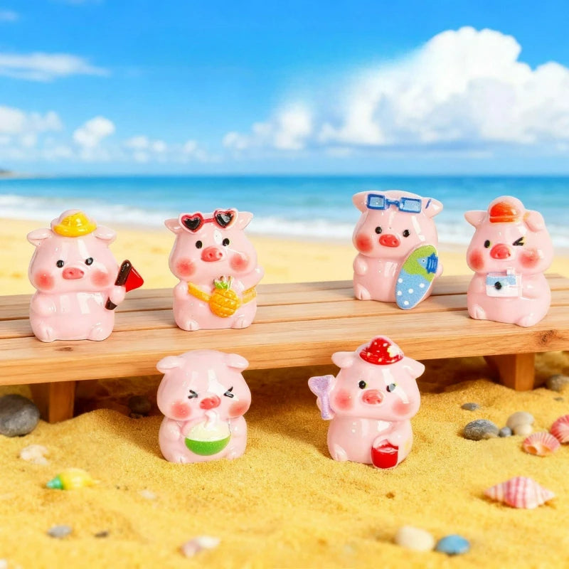 Colección de decoraciones en resina rosa con cerdo miniatura y accesorios sobre una tabla de madera en una playa arenosa.