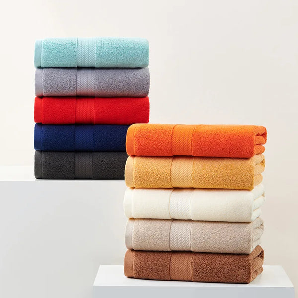 A stack of various colored premium 100% cotton quick-dry face towels in shades of blue, gray, red, orange, and beige.
