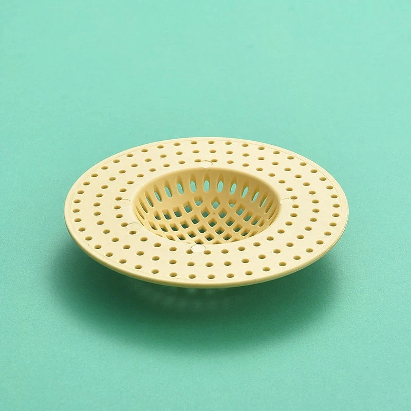 A round, light beige kitchen sink drain strainer and hair catcher with a perforated mesh design.