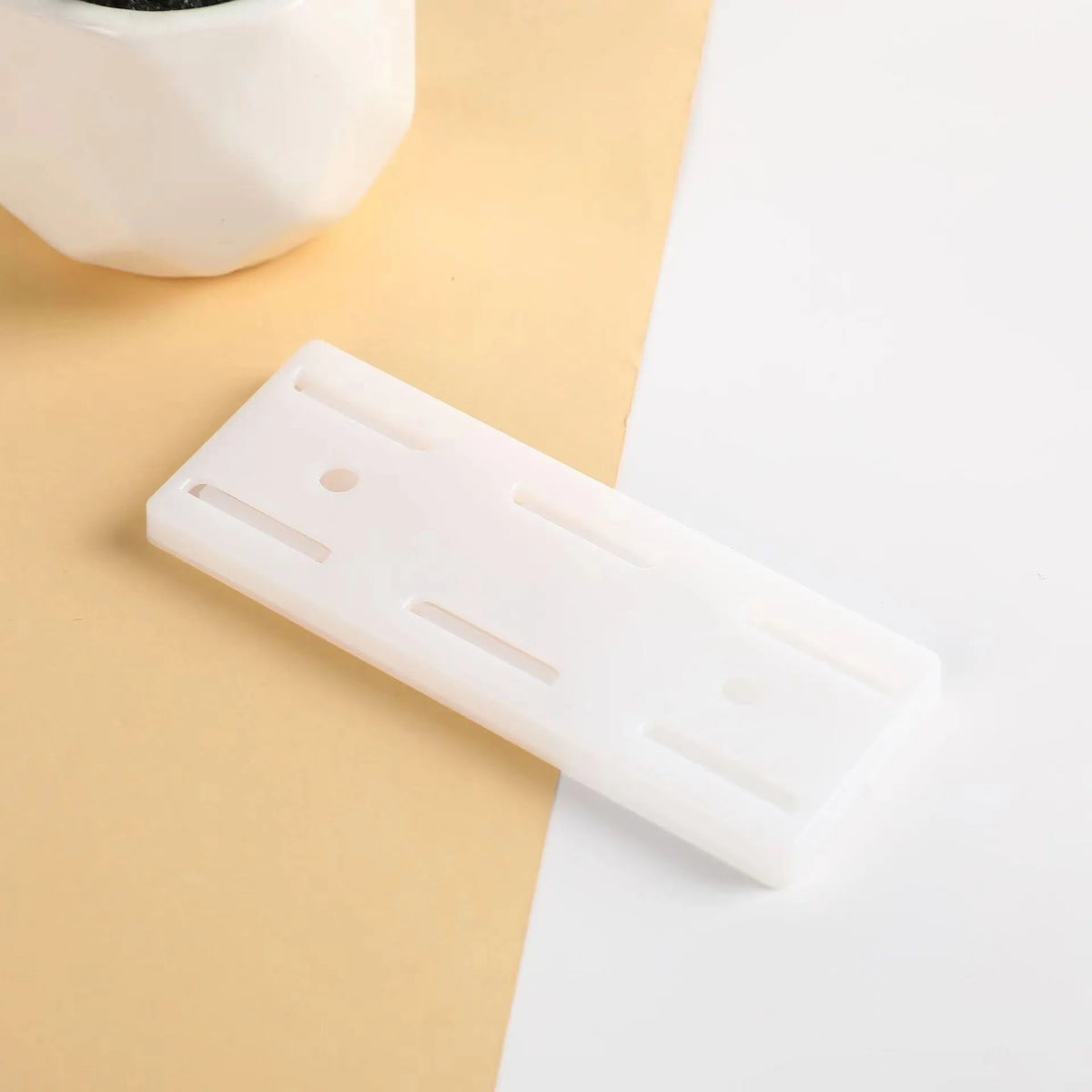 A white self-adhesive desktop cable organizer holder lying on a beige surface.