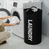 A black laundry basket with a padded handle is shown next to a white washing machine.