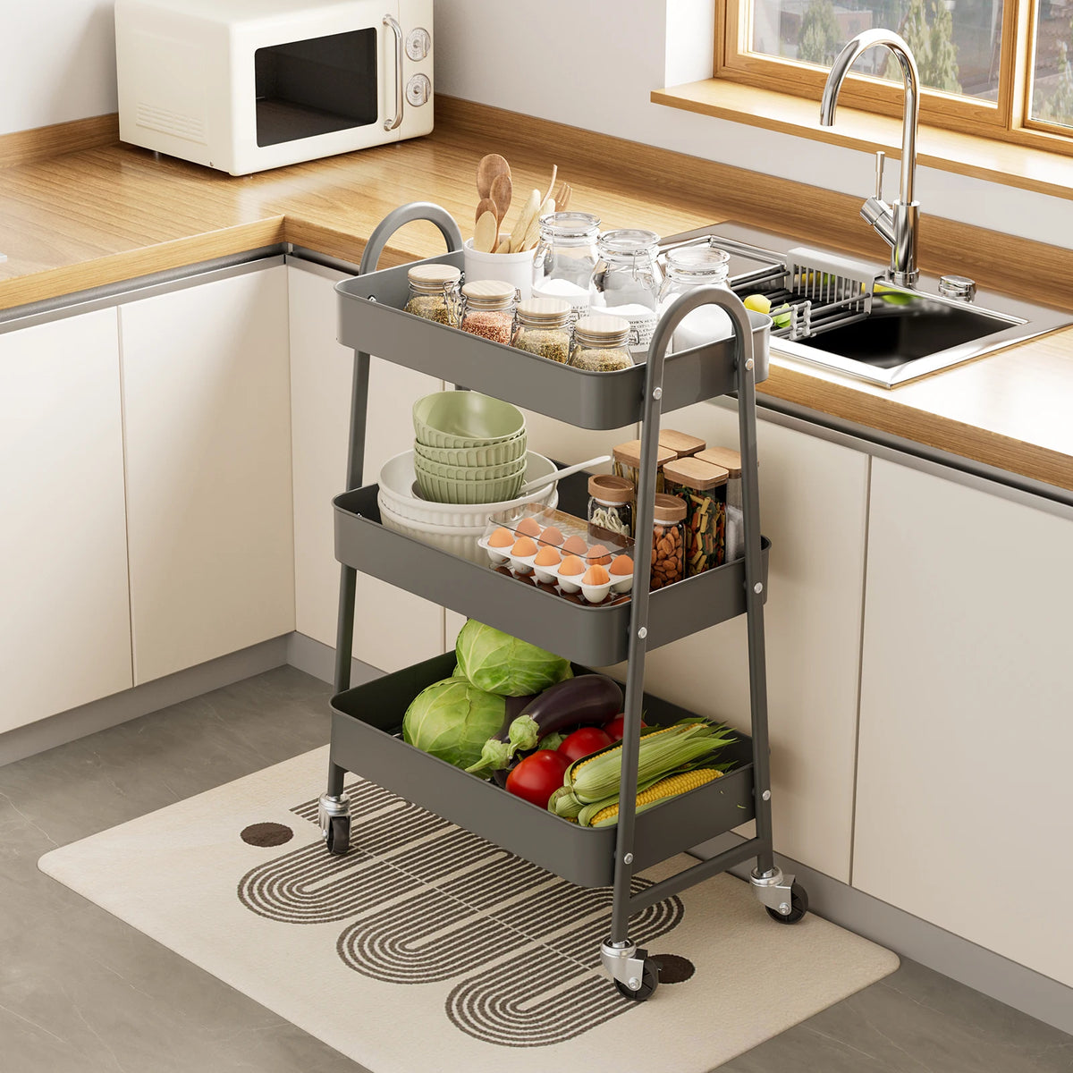 A three-tier metal rolling storage cart filled with various kitchen items is placed on a modern kitchen countertop.
