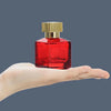 A clear glass perfume bottle with a red liquid and a gold cap is held in a person's hand.