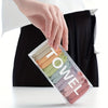 A hand is holding a clear plastic container filled with various colored disposable compressed washcloths or facial cleansing 