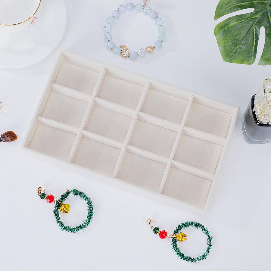 A rectangular velvet jewelry organizer tray with multiple compartments and several beaded bracelets is displayed on a white s