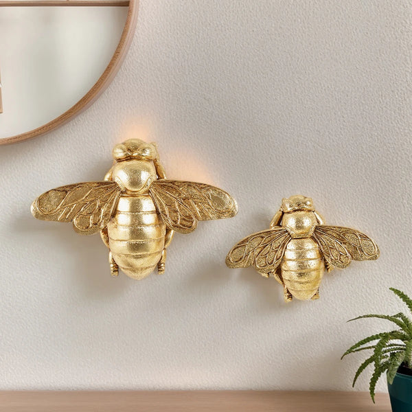 A golden bee wall decor piece mounted on a white wall.