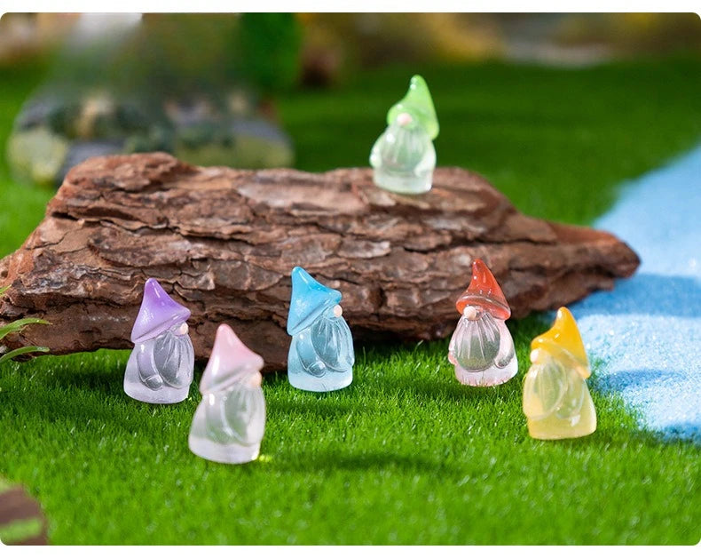 A collection of luminous resin mini fairy gnomes in various pastel colors sitting on green grass next to a brown log.