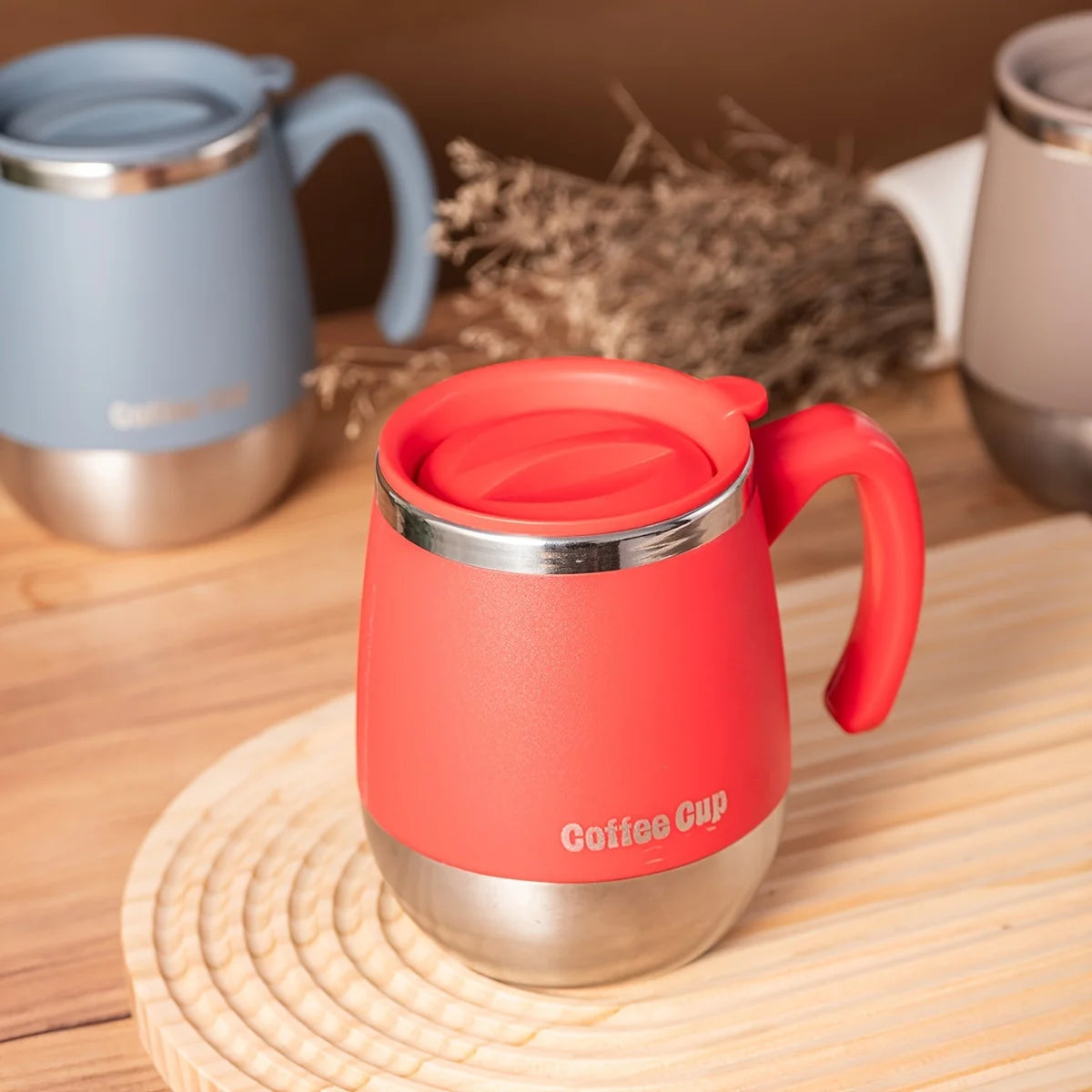 A bright orange insulated stainless steel coffee cup with a red lid sits on a wooden surface.
