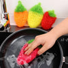 A hand is using a red strawberry scrubber sponge to clean food in a black frying pan.