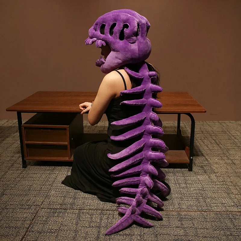 A person wearing a realistic purple dinosaur skeleton costume, seated in front of a wooden table.