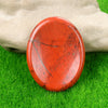 A smooth, oval, reddish-orange natural quartz thumb stone resting on green grass.