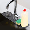 A chrome faucet is mounted on a black silicone mat, with a bottle of liquid soap and a green sponge visible.