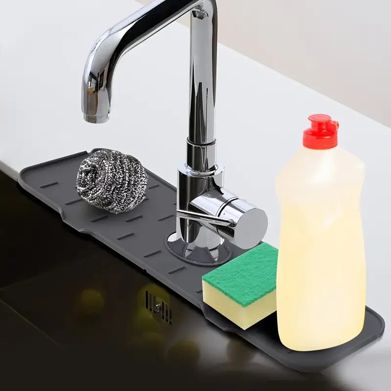 A chrome faucet is mounted on a black silicone mat, with a bottle of liquid soap and a green sponge visible.