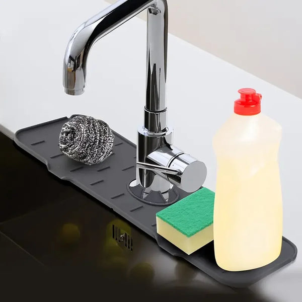 A chrome faucet is mounted on a black silicone mat, with a bottle of liquid soap and a green sponge visible.