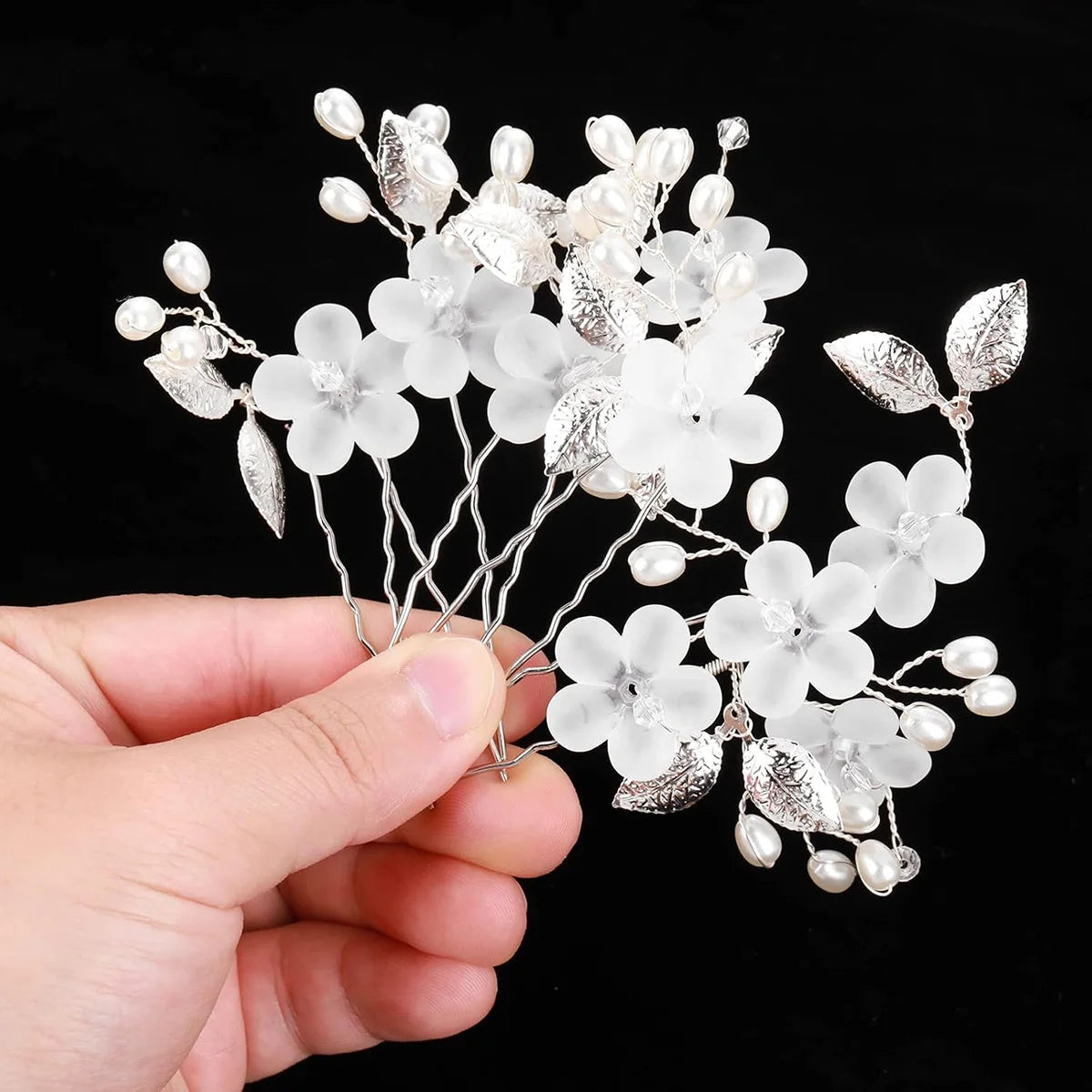 A set of pearl and silver floral bridal hair clips displayed in a hand.