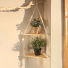 A boho triangle floating wall shelf displaying potted greenery against a light beige wall.