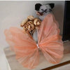 A pink sheer fabric butterfly decoration with gold floral accents and a small black and white animal figure.