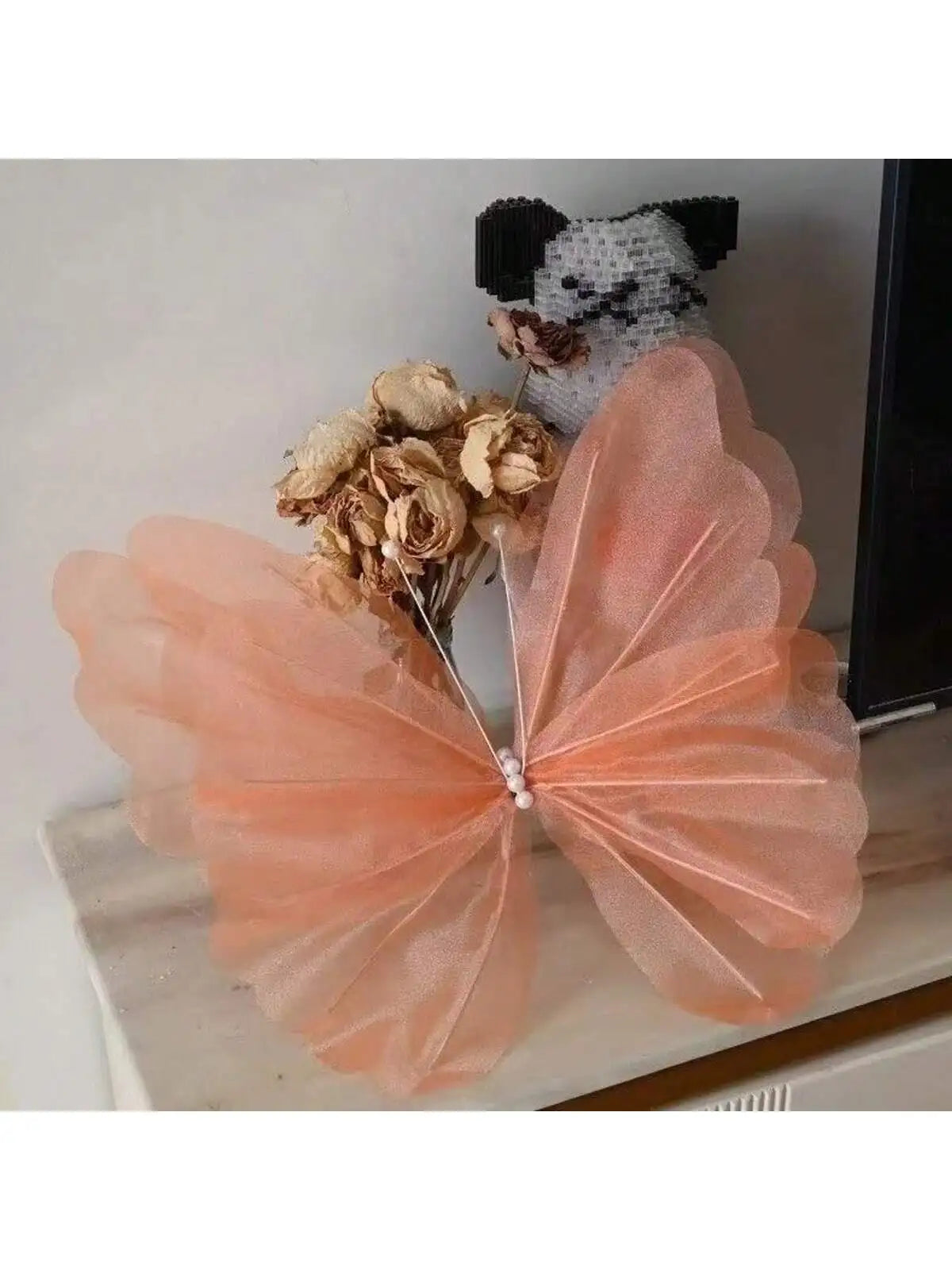 A pink sheer fabric butterfly decoration with gold floral accents and a small black and white animal figure.