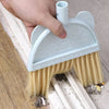 A hand is holding a light blue toddler mini broom and dustpan set against a wooden surface.