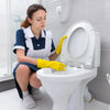 A woman wearing yellow gloves is cleaning a white toilet bowl with a pumice stone.