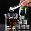 A hand holds a silver key above a glass of whiskey and several reusable stainless steel ice cubes.